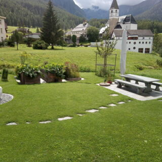Gartenanlage aus Steintisch, Steinbrunnen, Hochbeet und grüner Wiese in Tarasp im Engadin.